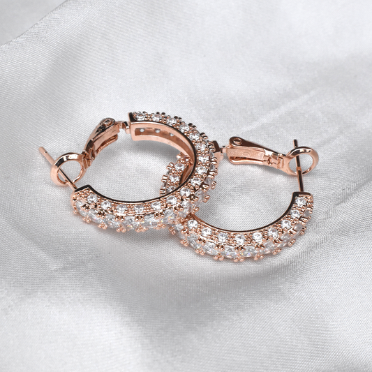 A pair of rose gold filled hoop earrings featuring three rows of brilliant diamonte crystals on a white silk background.