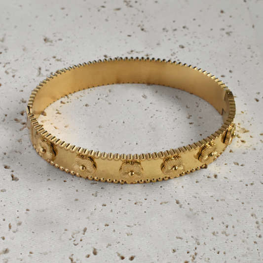 Close up of an 18k gold plated bangle bracelet featuring embossed vintage floral motifs and a textured beaded edge. Tarnish-free everyday jewelery.